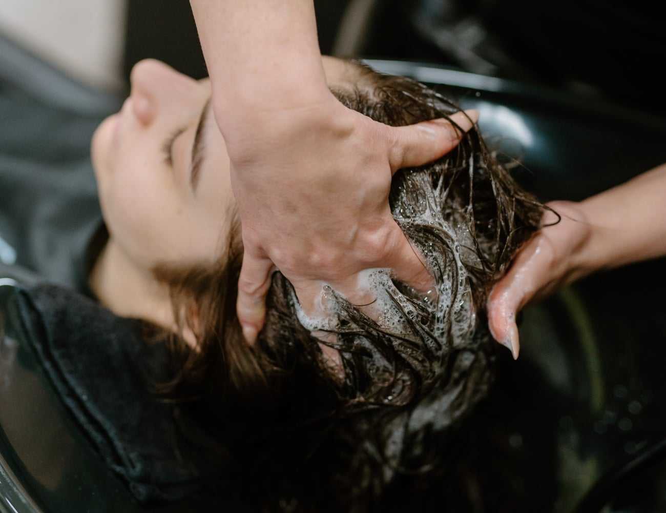 Person getting a shampoo at a salon, lying back with hands massaging their scalp.